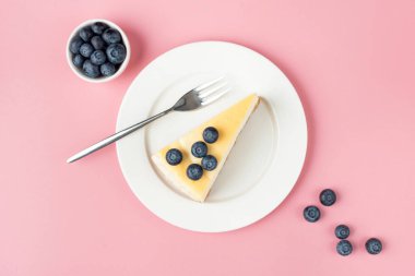 Pembe arka planda yaban mersinli cheesecake, üst manzara. Bir dilim peynirli kek.