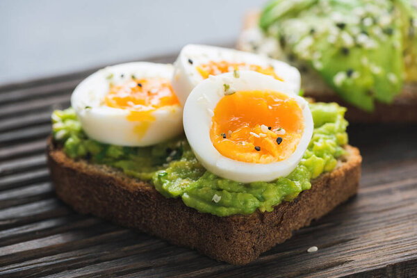 Avocado toast with egg on wooden board, closeup view