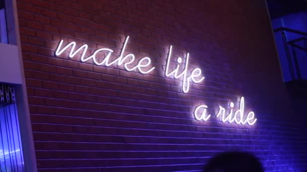 Make life a ride written in English in Neon on on a Brick wall with disco lights milling on it — стоковое видео