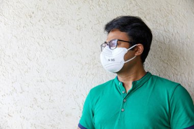 Yetişkin Güney Asyalı erkek yeşil tişört giyiyor ve N95 beyaz solunum cihazı var. Vücut ve Yüz kameradan bakıyor.