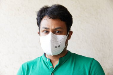Yeşil tişörtlü ve kameraya bakan Beyaz N95 Solunum Cihazı giyen yetişkin Hintli Erkek (Siyah gözler, N95 Maske, Beyaz Arkaplan, Doğal Işık, Mumbai, Hindistan, Hastalığın Korunması))
