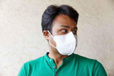 Orta yaşlı Güney Asyalı yetişkin erkek, N95 maskeli ve kameranın soluna bakıyor. Profil fotoğrafı... Kirlilik önleyici, Coronavirus, Beyaz Maske, Yeşil Gömlek, Tombul, Siyah Saçlı, Koruyucu)