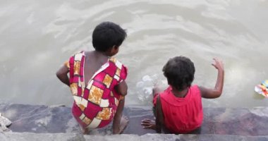 10 yaşın altındaki iki küçük kızın el kamerasıyla çekilmiş bir fotoğrafı. Birbirleriyle oynuyorlar ve sonra elbiselerini Kolkata 'daki Hooghly Nehri kıyısında yıkıyorlar. 17 Sep 2020.