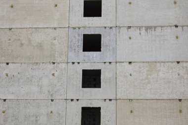 Çok katlı bir binanın beton gri duvarı. Camsız pencereler. İnşaat halindeki bir binanın duvarı