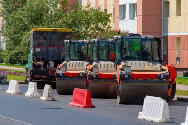 Üç silindirli ve bir asfalt kaldırım kaldırım kaldırımı yeni bir yol yatağı hazırlama çalışmalarının başlamasını bekliyor. Şehir sokaklarının tamiri.