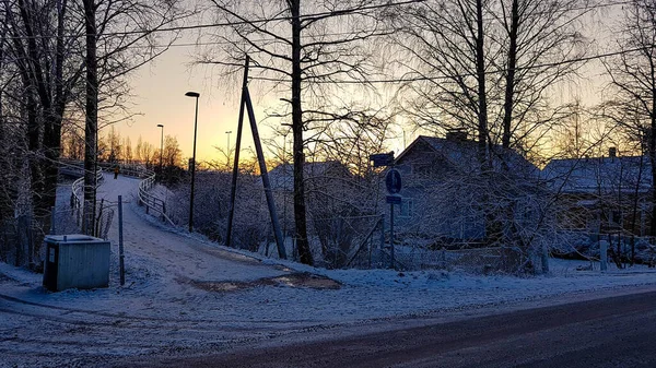 stock image Winter sunset landscape with snow, trees, wooden houses and a pedestrian bridge.