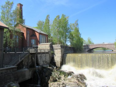 Su, kırmızı tuğladan binaları olan tarihi küçük bir su santralinden akıyor..