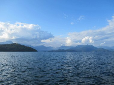 Vancouver yakınlarındaki mavi gökyüzünde deniz, dağlar ve beyaz bulutlarla güzel bir manzara..