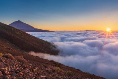 Batan güneşin bulutların arasında gözlük. Günbatımı Teide Volkanı Milli Parkı içinde. 