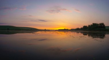 çayırlar ve alanları ile çevrili bir göl üzerinde gündoğumu