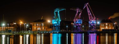 Szczecin, Poland - December 2018: Illuminated old port cranes on boulevard at night clipart