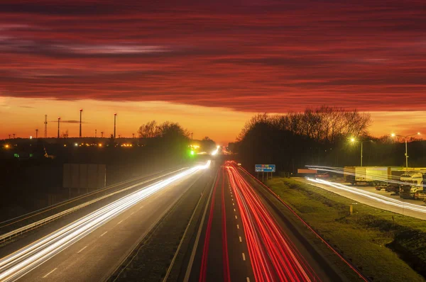 As trilhas de luz na auto-estrada durante um pôr do sol dramático — Fotografia de Stock