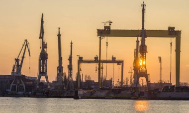 Siluetleri Vinçler ve Portal vinçler batan güneşin ışığında. Szczecin Tersanesi