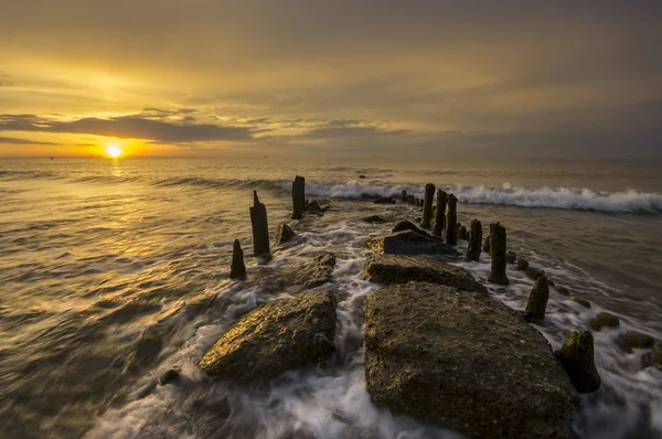 Um quebra-mar que quebra as ondas ao pôr-do-sol — Fotografia de Stock