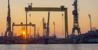 Siluetleri Vinçler ve Portal vinçler batan güneşin ışığında. Szczecin Tersanesi