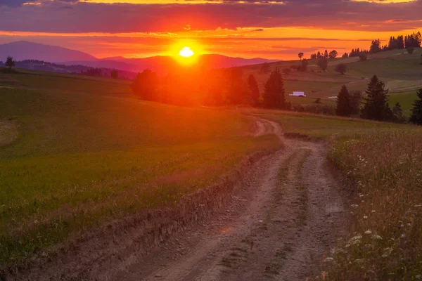 Sunset over a mountain road leading through meadows — Stock Photo, Image