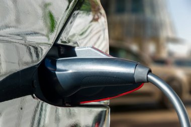 Elektrikli araba, şehir caddesinde elektrikli araba şarj istasyonuyla park yerinde şarj oluyor. Şarj olan elektrikli arabaya takılan güç kaynağını kapat.