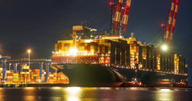 Geceleyin bir limandaki konteynır terminaline büyük bir konteyner gemisi boşaltılıyor.