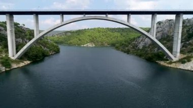 Sibenik Köprüsü 'nün havadan görüntüsü. Hırvatistan, Avrupa 'daki Krka nehri üzerindeki otoban köprüsünün altında uçan insansız hava aracı. Arka planda güzel Akdeniz manzarası, tekneler, yatlar, yelkenliler ve sürat tekneleri.