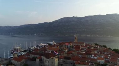 Korcula adasının ortasındaki kulede sallanan Hırvat bayrağı, 4K hava manzaralı. Günaydın, Korcula manzarası ve limana demirlemiş lüks yatlar ve yelkenliler..