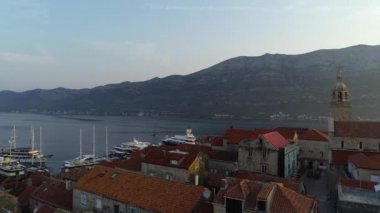 Korcula adasının ortasındaki kulede sallanan Hırvat bayrağı, 4K hava manzaralı. Günaydın, Korcula manzarası ve limana demirlemiş lüks yatlar ve yelkenliler..