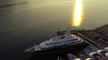 Lüks büyük beyaz bir yat limanda ya da limanda, gün batımında ya da gün doğumunda hava manzaralı. Yaz mevsiminde güzel yeşil bir ada. Yat haftasında yelkencilik deneyimi.
