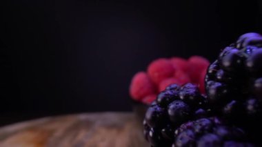 Siyah kaselerde taze orman meyveleri. Siyah arkaplanda böğürtlen, böğürtlen, ahududu. Seçici odaklı, yavaş çekim odaklı sonda mercek dolly alışılmadık görünümü. 