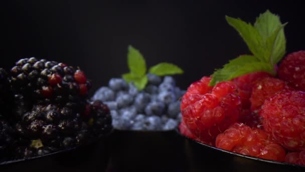 新鲜的森林水果在黑色的碗里 黑莓蓝莓黑碗里的覆盆子黑底具有选择性聚焦 慢动作的探光镜异型视点 — 图库视频影像