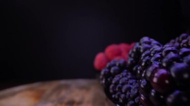 Siyah arka planda böğürtlen, böğürtlen, ahududu. Seçici odaklı sonda mercek dolly alışılmadık görünümü. Tahta masadaki taze orman meyveleri..
