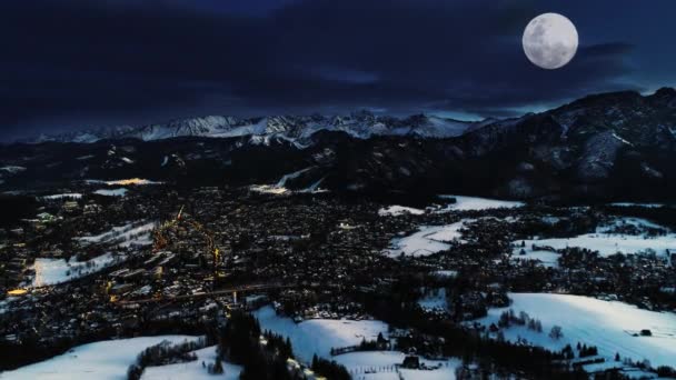 山の冬の夜 空中ビューです 魔法の冬 クリスマスの風景 白い山 スキー場 大きな輝く月で覆われた輝く高山都市 夜のザコパネ — ストック動画