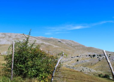 Arka planda dağ çölü olan kırık dikenli tel örgü. Bosna-Hersek 'in Bjelasnica Dağı yolunda.