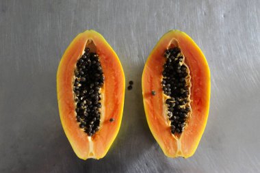 Papaya meyvesi mutfak masasında ikiye bölündü. Gri metal mutfak masası arka planı.