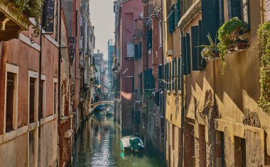 Renkli tarihi evleri, yaya köprüsü ve güneşli bir kış gününde demirlemiş tekneleri olan pitoresk bir Venedik kanalı.