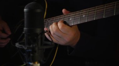 Mikrofonun yanındaki stüdyoda gitar çalan müzisyen.