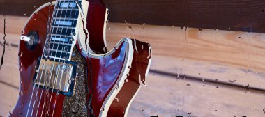 Su damlalarıyla birlikte cam arkasındaki tahtanın üzerinde elektro gitar var.