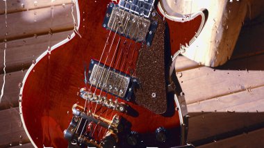 Su damlalarıyla birlikte cam arkasındaki tahtanın üzerinde elektro gitar var.