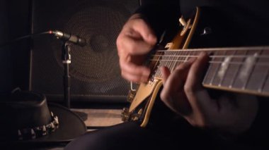 Mikrofonun yanındaki stüdyoda gitar çalan müzisyen.