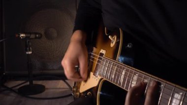 Mikrofonun yanındaki stüdyoda gitar çalan müzisyen.