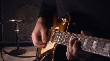 Mikrofonun yanındaki stüdyoda gitar çalan müzisyen.