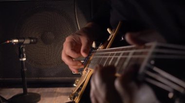 Mikrofonun yanındaki stüdyoda gitar çalan müzisyen.