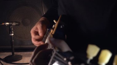 Mikrofonun yanındaki stüdyoda gitar çalan müzisyen.