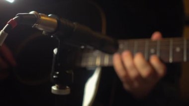 Mikrofonun yanındaki stüdyoda gitar çalan müzisyen.
