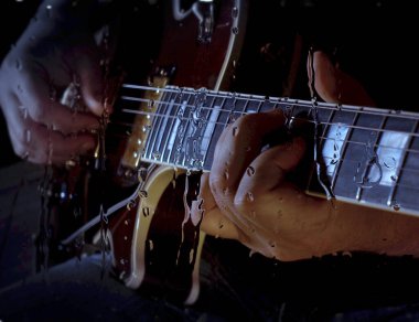 Müzisyen, bardağın arkasındaki mikrofonun yanındaki stüdyoda su damlalarıyla gitar çalıyor.