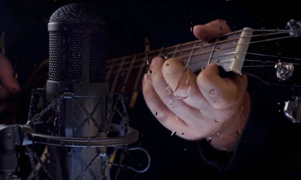 Musician plays guitar at studio near the microphone behind the glass with water drops