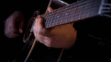 Müzisyen, bardağın arkasındaki mikrofonun yanındaki stüdyoda su damlalarıyla gitar çalıyor.