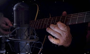 Müzisyen, bardağın arkasındaki mikrofonun yanındaki stüdyoda su damlalarıyla gitar çalıyor.