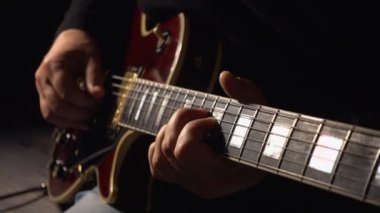 Müzisyen stüdyoda gitar çalar. Yakın plan. Koyu arkaplan