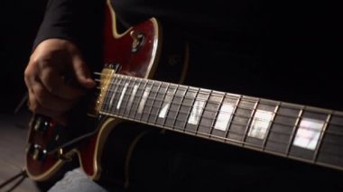 Müzisyen stüdyoda gitar çalar. Yakın plan. Koyu arkaplan