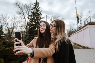 İki güzel genç kız parkta yürürken selfie çekiyorlar..