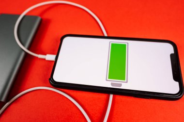 Kırmızı arkaplanda akıllı telefon ve ekranda düşük pil simgesi.